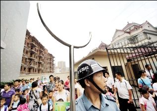 學校門口，保安頭戴鋼帽手拿鋼叉站在校門口，護衛學校安全。